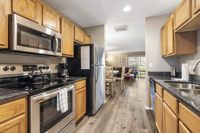 kitchen with light wood-style flooring, visible vents, a sink, dark stone countertops, and appliances with stainless steel finishes