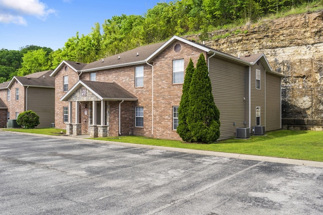 view of front of home with central air condition unit, brick siding, and a front yard
