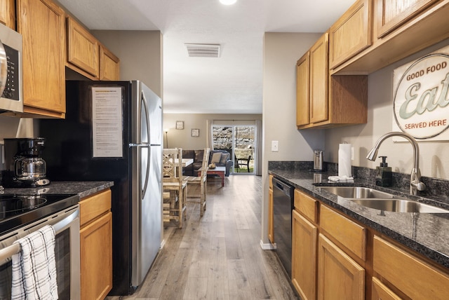 kitchen with dark stone countertops, a sink, light wood-type flooring, visible vents, and appliances with stainless steel finishes