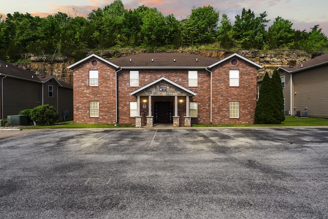 view of front of home with central AC, brick siding, and uncovered parking