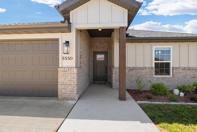 doorway to property featuring a shingled roof, board and batten siding, brick siding, and an attached garage