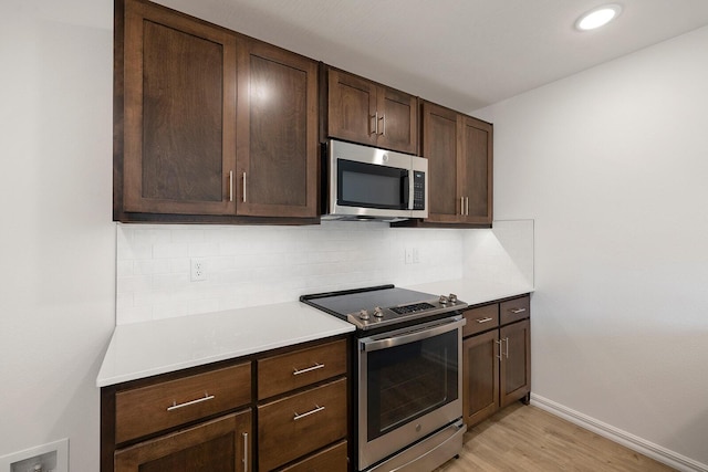 kitchen featuring light wood finished floors, dark brown cabinets, backsplash, light countertops, and appliances with stainless steel finishes