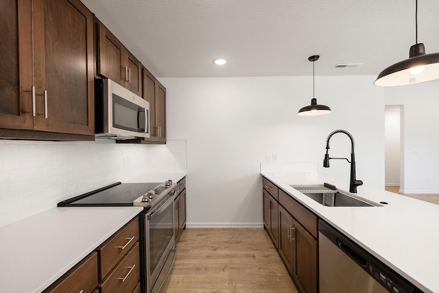 kitchen with a sink, appliances with stainless steel finishes, light countertops, light wood-style floors, and tasteful backsplash