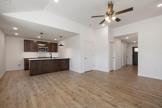 kitchen featuring a ceiling fan, light wood-style flooring, dark brown cabinets, stainless steel microwave, and open floor plan