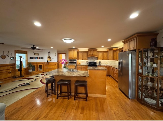 kitchen featuring appliances with stainless steel finishes, brown cabinetry, a kitchen breakfast bar, light wood-style floors, and an island with sink