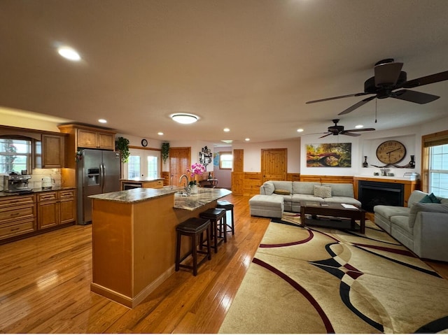 kitchen with recessed lighting, light wood finished floors, stainless steel fridge with ice dispenser, a kitchen breakfast bar, and dark countertops