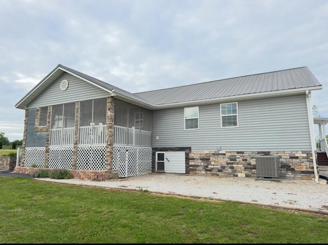 back of property with stone siding, cooling unit, a sunroom, metal roof, and a lawn