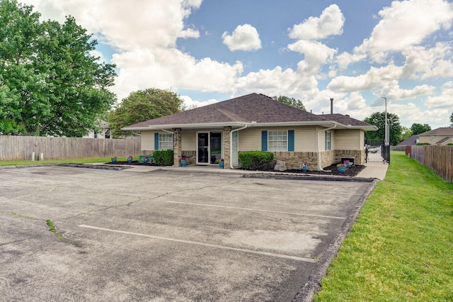 view of front of house featuring stone siding, uncovered parking, fence, and a front lawn