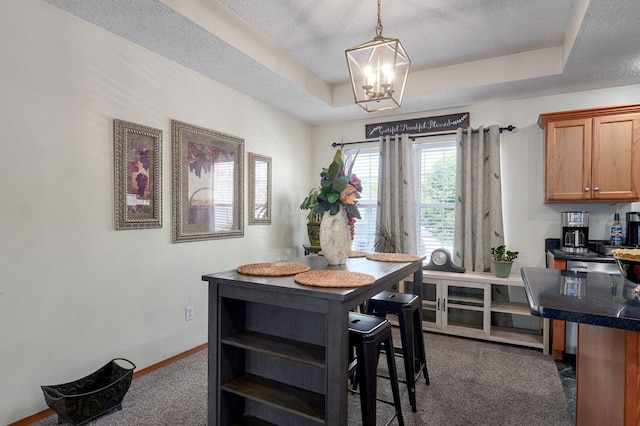 dining space featuring a textured ceiling, an inviting chandelier, a tray ceiling, baseboards, and dark carpet