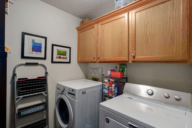 clothes washing area with washing machine and dryer, a textured ceiling, and cabinet space