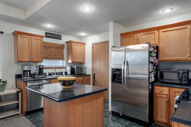 kitchen with a sink, dark countertops, stainless steel appliances, a textured ceiling, and a kitchen island