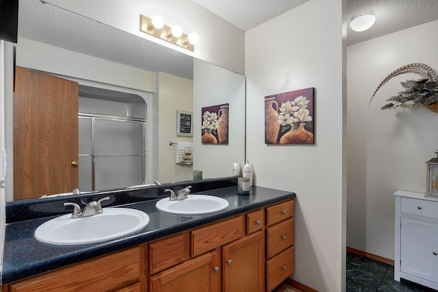 bathroom featuring double vanity, a textured ceiling, a shower stall, and a sink