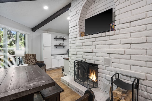 living room featuring light wood-type flooring, visible vents, a fireplace, and lofted ceiling with beams