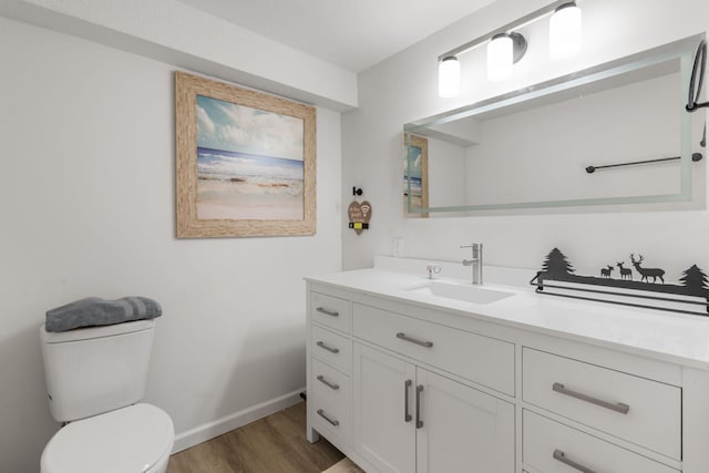 half bath with toilet, baseboards, vanity, and wood finished floors