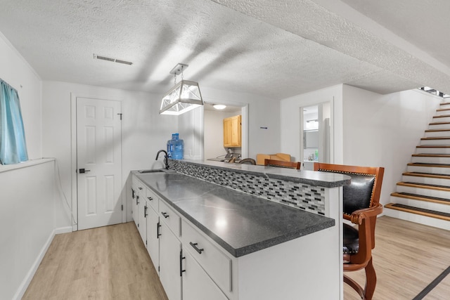 kitchen featuring a sink, a peninsula, visible vents, light wood-style flooring, and dark countertops