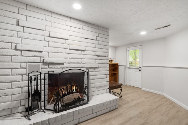 interior details featuring wood finished floors, a textured ceiling, visible vents, a fireplace, and baseboards