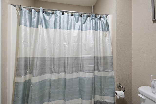 full bathroom with toilet, a textured wall, and a shower with curtain