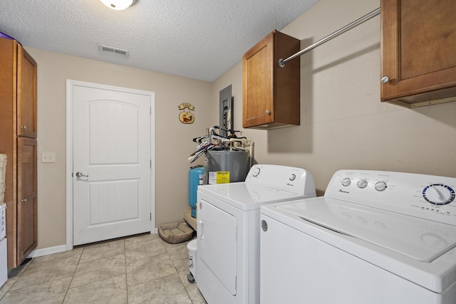 laundry room featuring a textured ceiling, visible vents, electric water heater, separate washer and dryer, and cabinet space