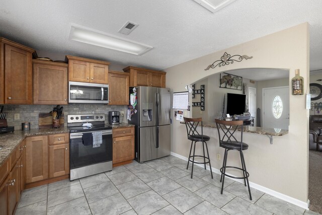 kitchen with a kitchen bar, brown cabinetry, arched walkways, appliances with stainless steel finishes, and tasteful backsplash