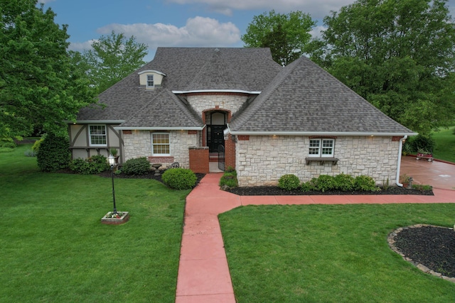 french country style house with stone siding, roof with shingles, and a front yard