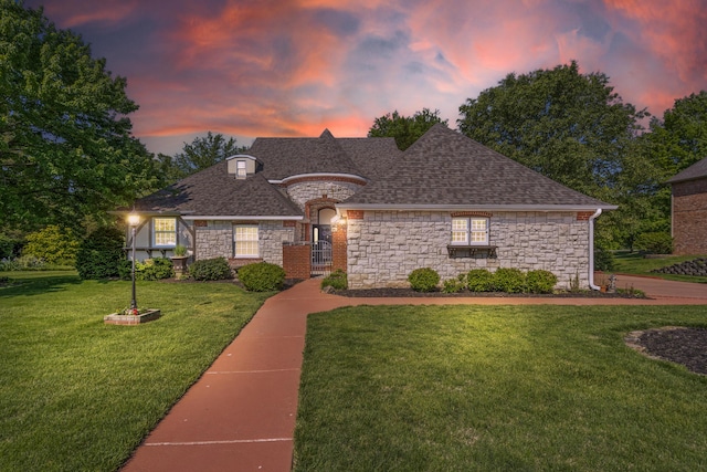 french provincial home featuring stone siding, a yard, and a shingled roof