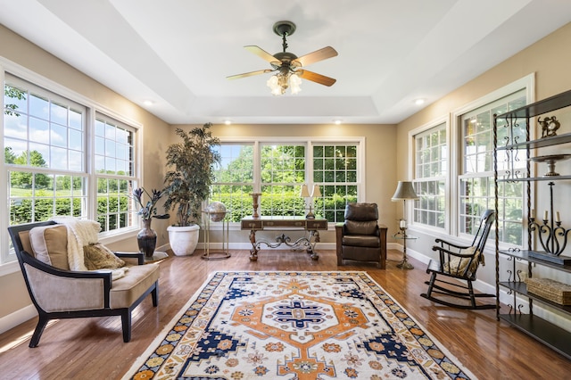 living area with a tray ceiling, wood finished floors, baseboards, and ceiling fan