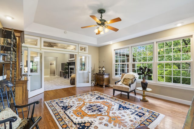 sitting room with a tray ceiling, ceiling fan, baseboards, and wood finished floors