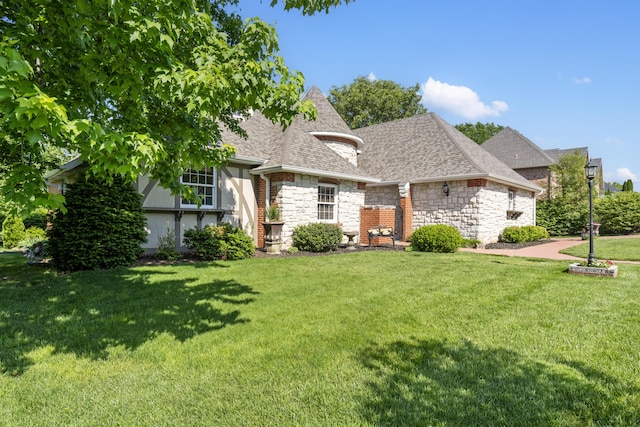 french provincial home featuring a front lawn, stone siding, and a shingled roof