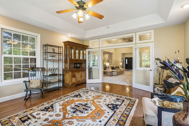 sitting room with french doors, a tray ceiling, a ceiling fan, and wood finished floors