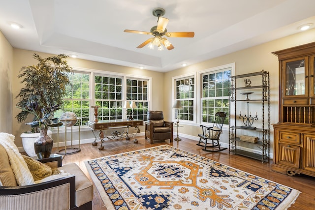 living area featuring a raised ceiling, ceiling fan, wood finished floors, baseboards, and recessed lighting