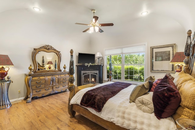 bedroom with wood finished floors, a warm lit fireplace, lofted ceiling, recessed lighting, and a ceiling fan