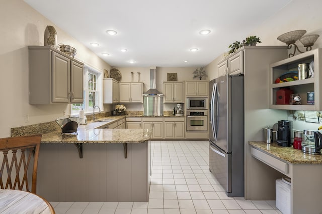 kitchen with appliances with stainless steel finishes, wall chimney exhaust hood, a peninsula, a sink, and light stone countertops