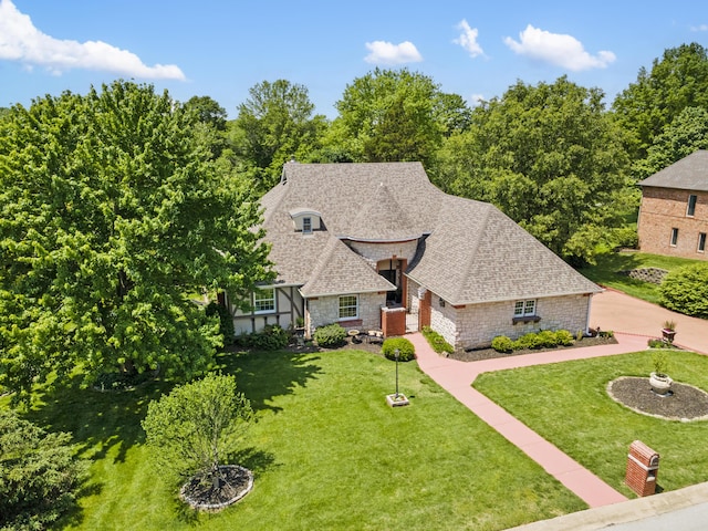 french country inspired facade with stone siding, a shingled roof, and a front lawn