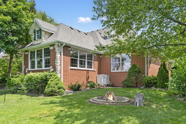 view of front of house featuring brick siding, a fire pit, a shingled roof, and a front yard