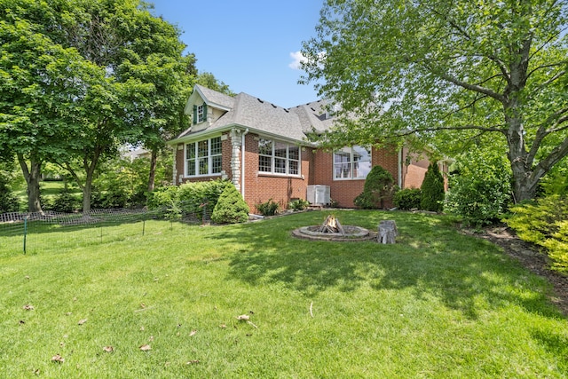 view of front facade with brick siding, an outdoor fire pit, central AC unit, and a shingled roof