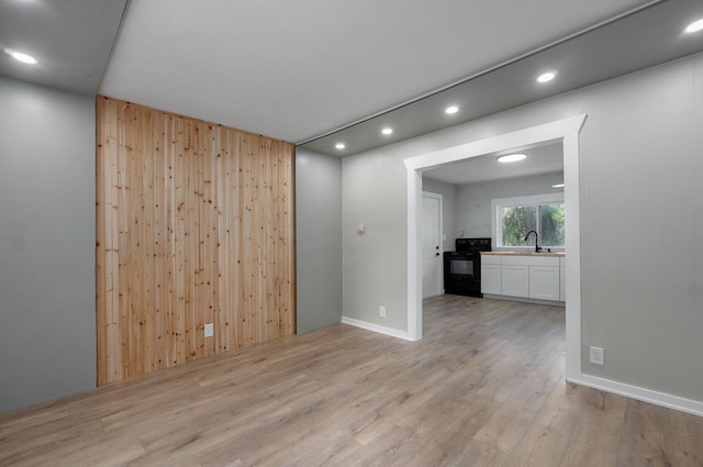 spare room with recessed lighting, light wood-type flooring, wooden walls, and a sink