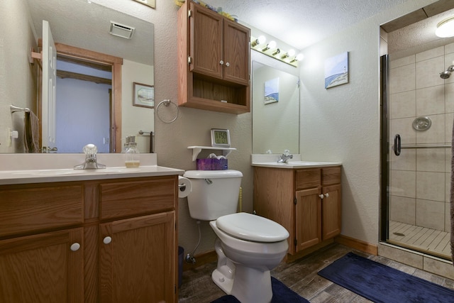 bathroom featuring toilet, wood finished floors, a textured ceiling, a shower stall, and two vanities