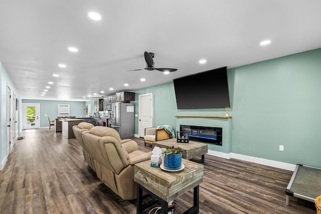 living room featuring baseboards, recessed lighting, dark wood-style flooring, a ceiling fan, and a glass covered fireplace