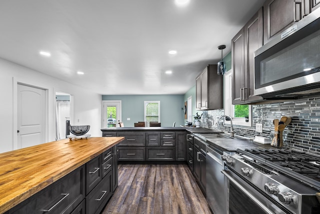 kitchen featuring appliances with stainless steel finishes, wood counters, dark wood-style floors, a sink, and backsplash
