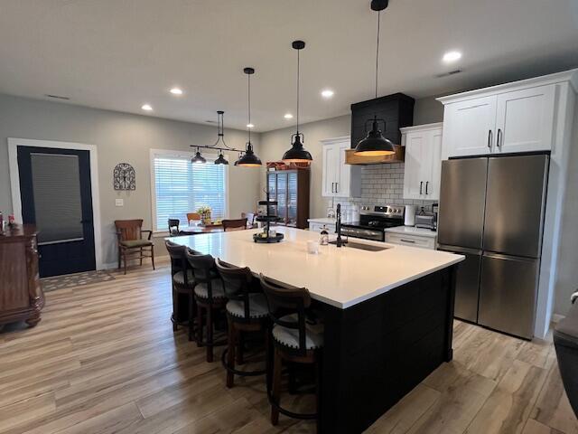 kitchen featuring appliances with stainless steel finishes, light wood-style floors, an island with sink, tasteful backsplash, and white cabinets