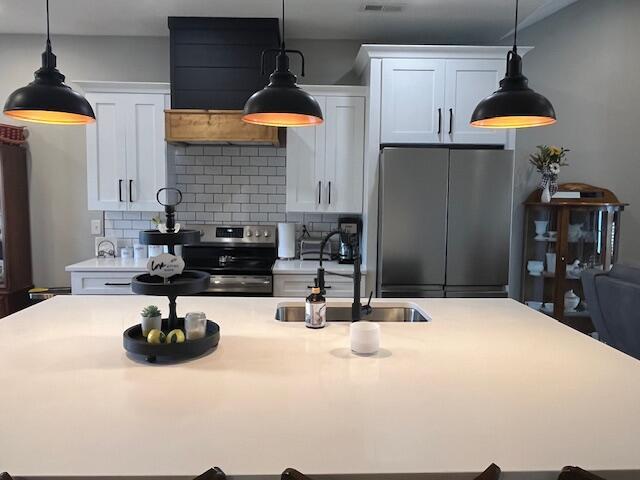 kitchen featuring stainless steel appliances, a sink, a kitchen island with sink, light countertops, and tasteful backsplash