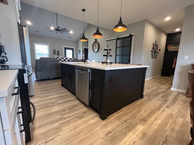 kitchen featuring a barn door, appliances with stainless steel finishes, ceiling fan, open floor plan, and light countertops