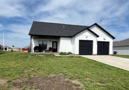 modern inspired farmhouse with driveway, a garage, a front yard, covered porch, and roof with shingles