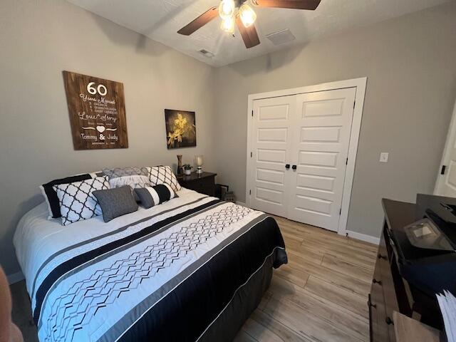 bedroom with light wood finished floors, a closet, ceiling fan, and baseboards