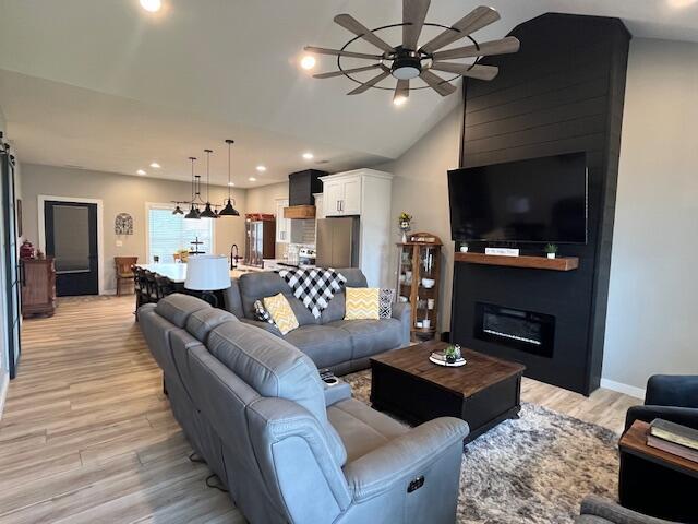 living room featuring ceiling fan, light wood finished floors, vaulted ceiling, recessed lighting, and a fireplace