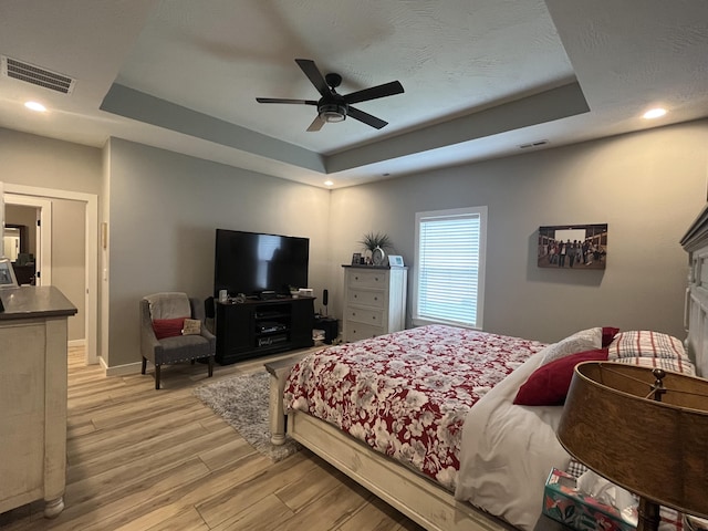 bedroom with a raised ceiling, light wood-type flooring, baseboards, a ceiling fan, and recessed lighting