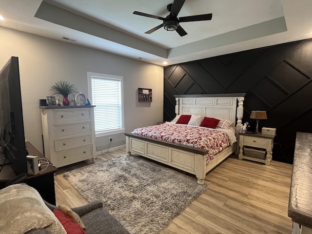 bedroom featuring light wood-style floors, a raised ceiling, baseboards, and a ceiling fan