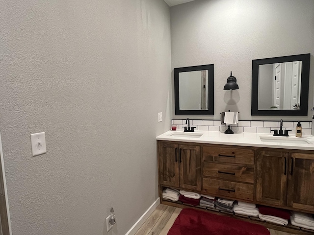 bathroom with wood finished floors, double vanity, backsplash, and baseboards