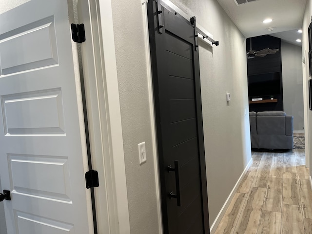 hall featuring a barn door, light wood-style floors, baseboards, and recessed lighting