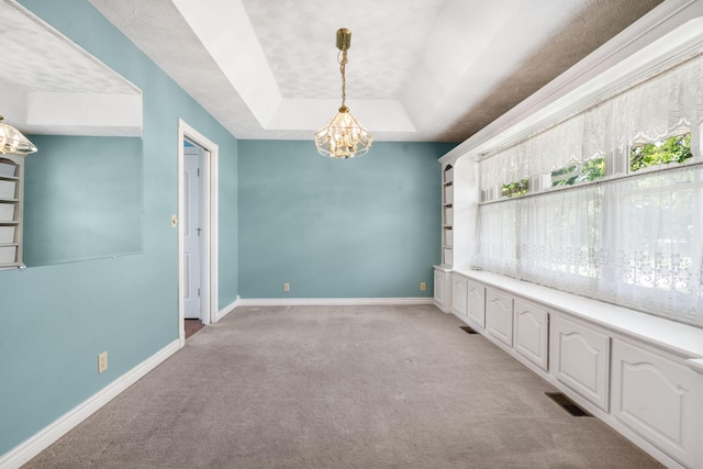 unfurnished dining area with light colored carpet, a chandelier, a tray ceiling, and baseboards